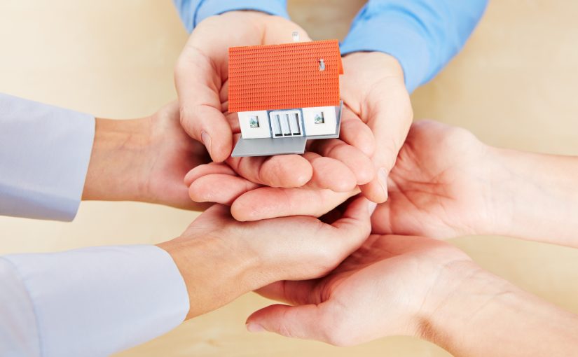 Viele Hände halten ein kleines Haus als Symbol für Sicherheit