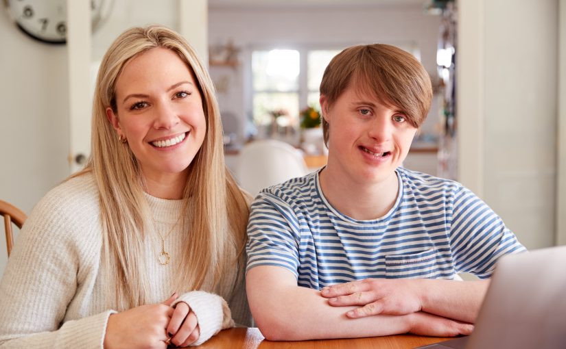 Junge mit Downsyndrom und junge Frau lächeln in die Kamera